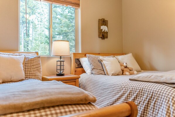 A bedroom with two beds, a nightstand with a lamp, and a wall decoration. - PET-FRIENDLY FOREST RETREAT CABIN | HOT TUB, FIRE-PIT, & A/C (Duck Creek Village)