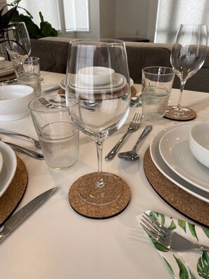 Une table à manger dressée avec de la vaisselle en verre transparent, des assiettes et des couverts, agrémentée de sous-verres en liège et d’une serviette à motifs.