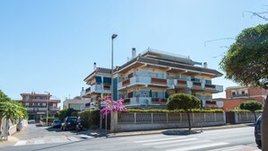 A multi-story residential building with balconies, a gated entrance, and a crosswalk in front. - Cosy apartment for 4 guests with WIFI, TV and terrace (Torvaianica)