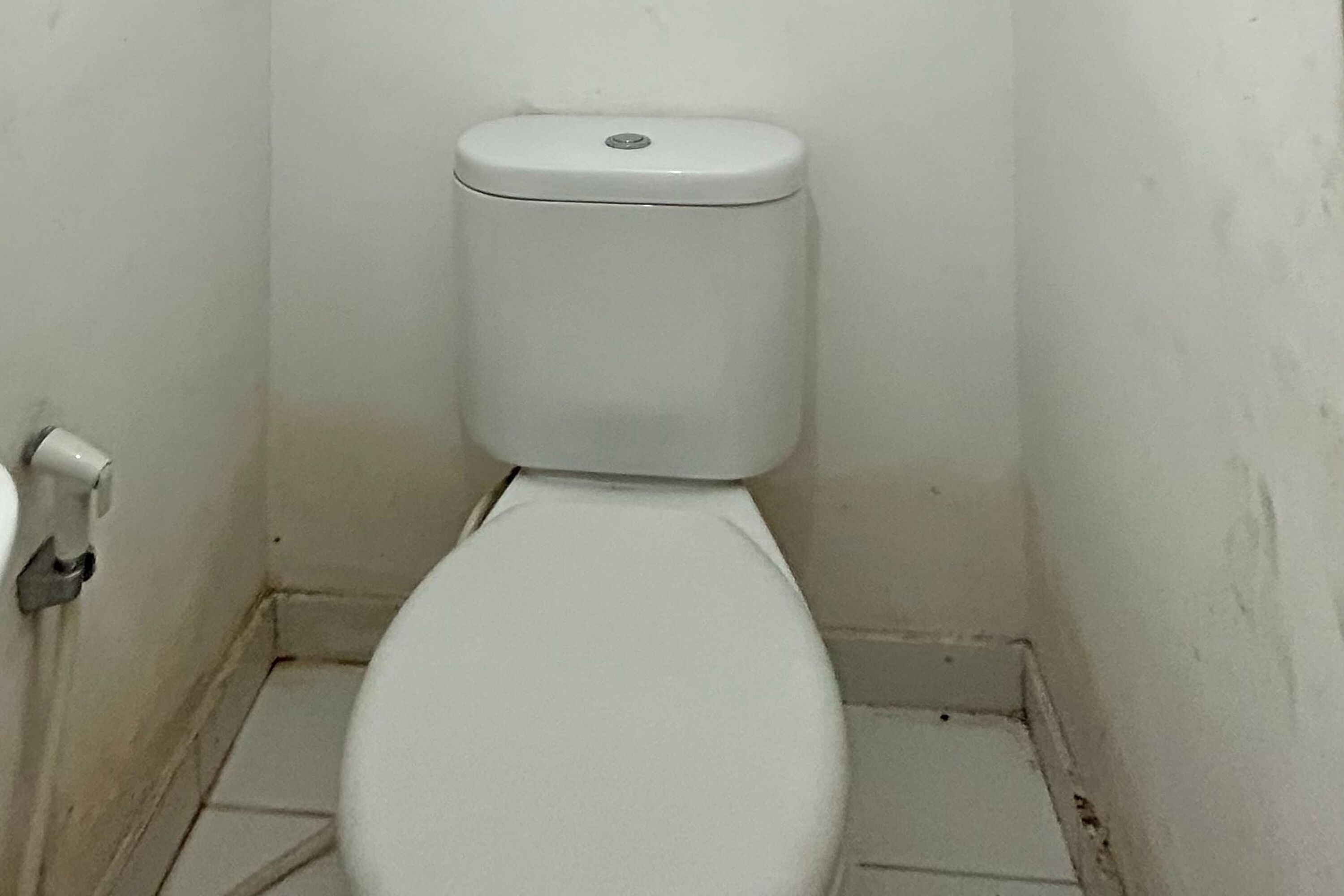 Eine kleine, weiße Toilette in einem schmalen Badezimmer mit weißen Wänden und Fliesenboden.