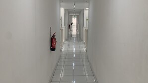 Un pasillo largo y estrecho con paredes blancas y suelo de baldosas. Un extintor está montado en la pared a la izquierda.