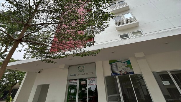 Entrada de un hotel con un letrero que dice "Beroda Lucent Hotel", un área de estar techada al aire libre y un árbol en primer plano.