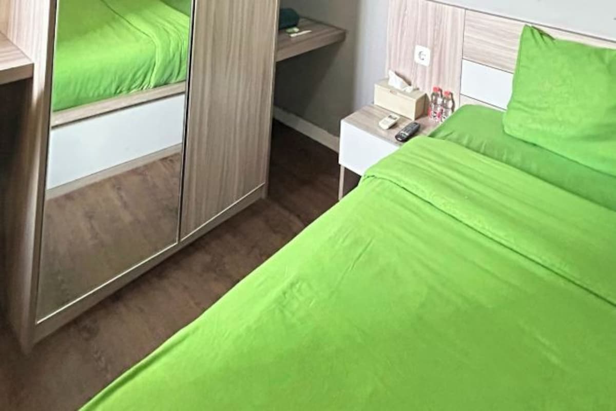 A hotel room with a bed, a bedside table with a remote control, and a mirror.