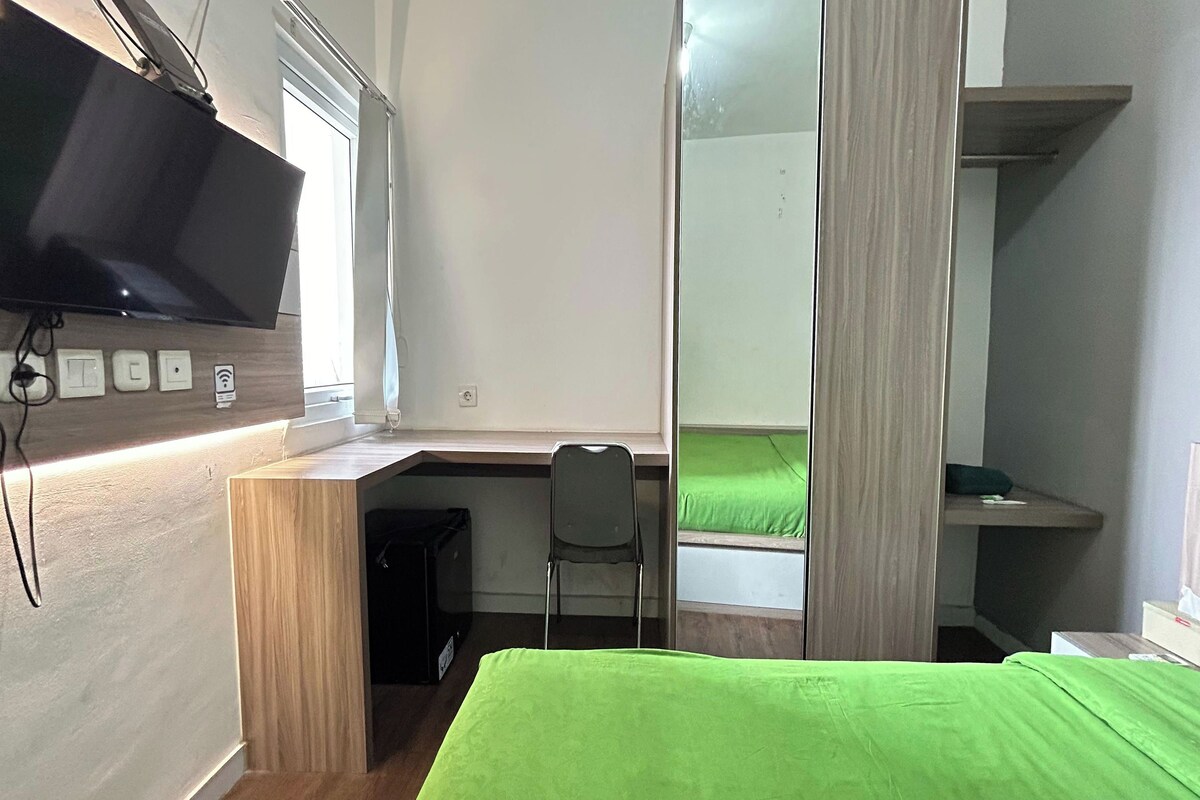 Una habitación pequeña con cama, escritorio, silla, televisor y espejo.