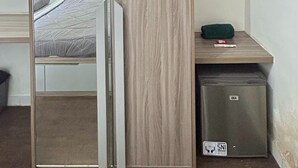 Una habitación pequeña con una cama, un escritorio de madera y un refrigerador GEA.