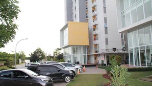 Un edificio moderno con una sección amarilla, un estacionamiento con varios coches y un césped bien cuidado.