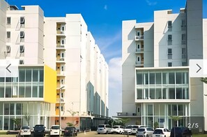 Un immeuble d’appartements moderne, doté de plusieurs étages, de grandes fenêtres et d’un espace de stationnement où sont garées plusieurs voitures.
