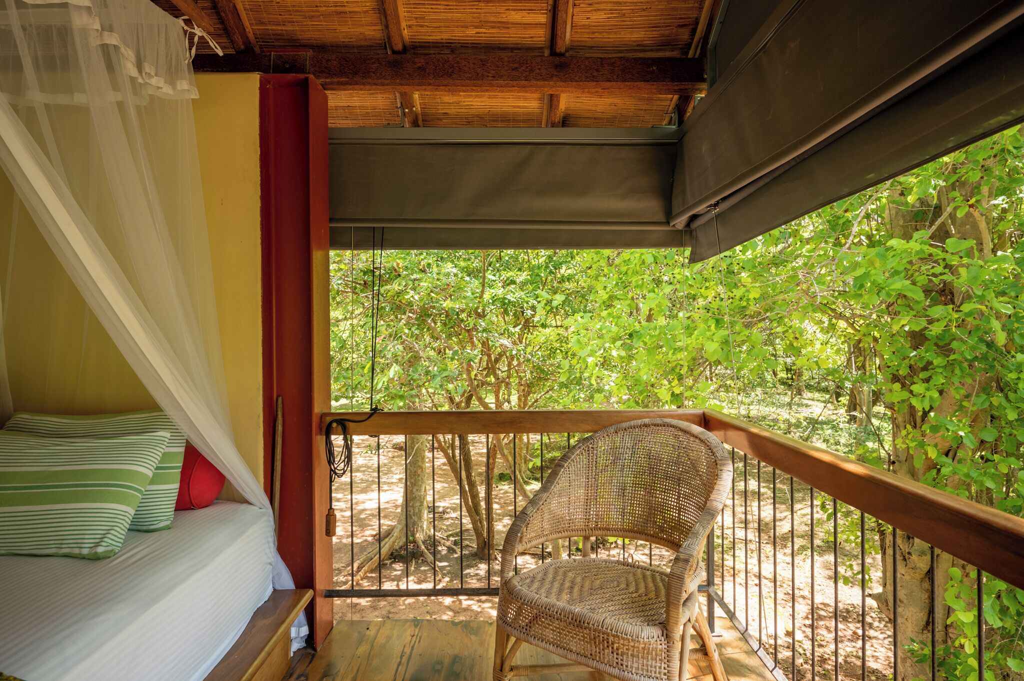 A balcony with a wicker chair, a bed with striped pillows, and a canopy.