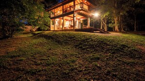 A two-story wooden house with a balcony, surrounded by trees and a grassy yard. - The River House Dambulla by The Serendipity Collection (Dambulla)