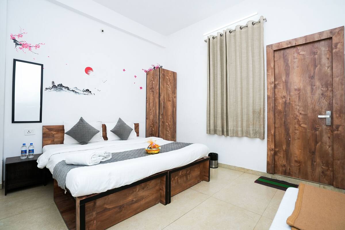 Une chambre à coucher avec un lit en bois, une table de chevet avec des bouteilles d’eau, une armoire et une grande porte en bois.