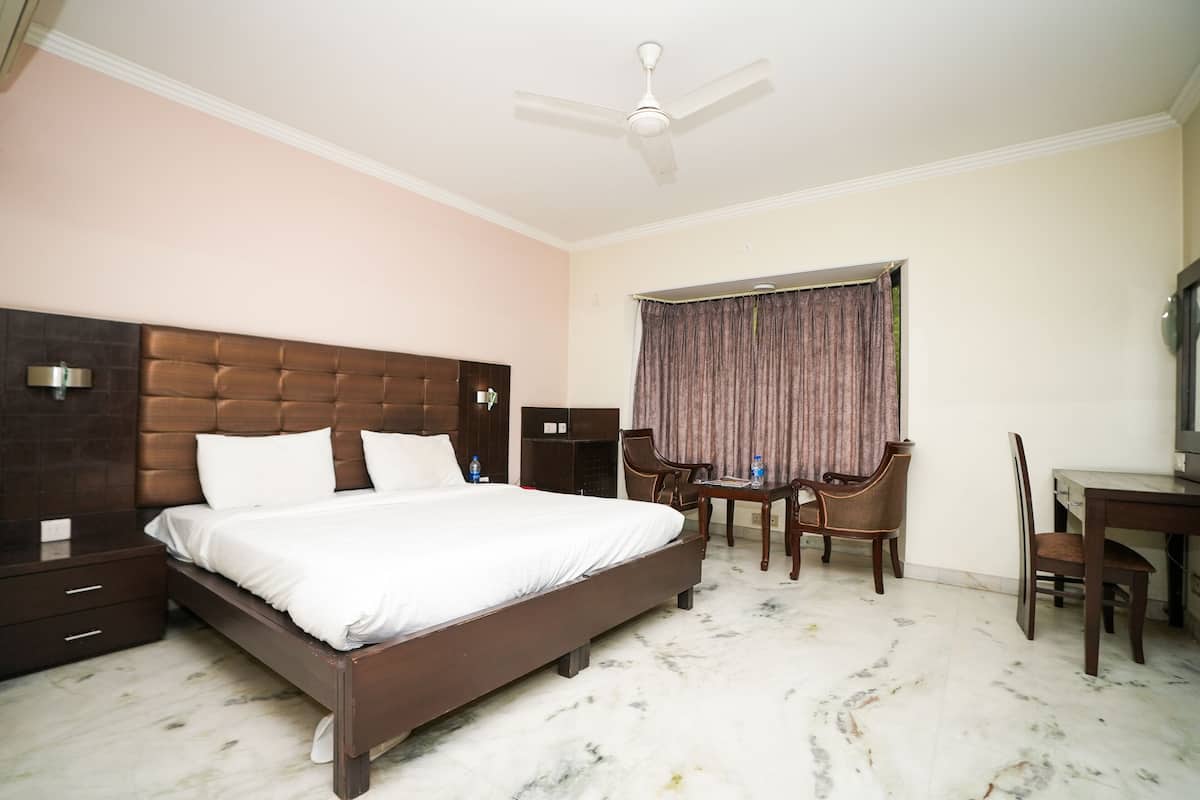A hotel room with a large bed, a desk, two chairs, a ceiling fan, and a window with curtains.