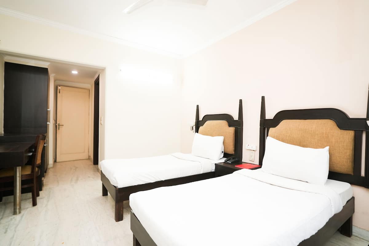 A hotel room with two single beds, a desk, and a chair.