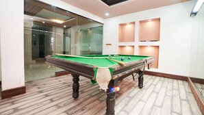Mesa de bilhar numa sala com chão de madeira, paredes de vidro e iluminação embutida.