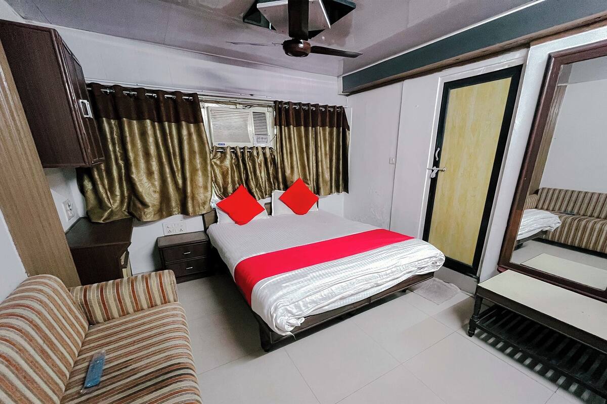 Una habitación de hotel con cama, sofá, mesita de noche, armario y espejo.