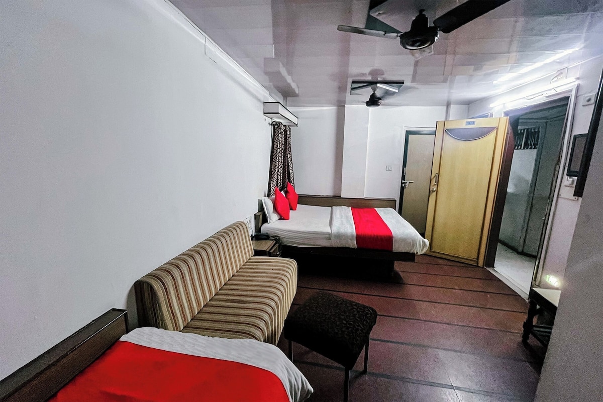 Habitación de hotel con sofá, dos camas individuales, una mesita, ventilador de techo y armario.