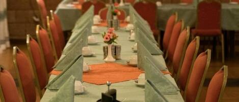 A long dining table with chairs, set with white plates, cups, and a centerpiece.