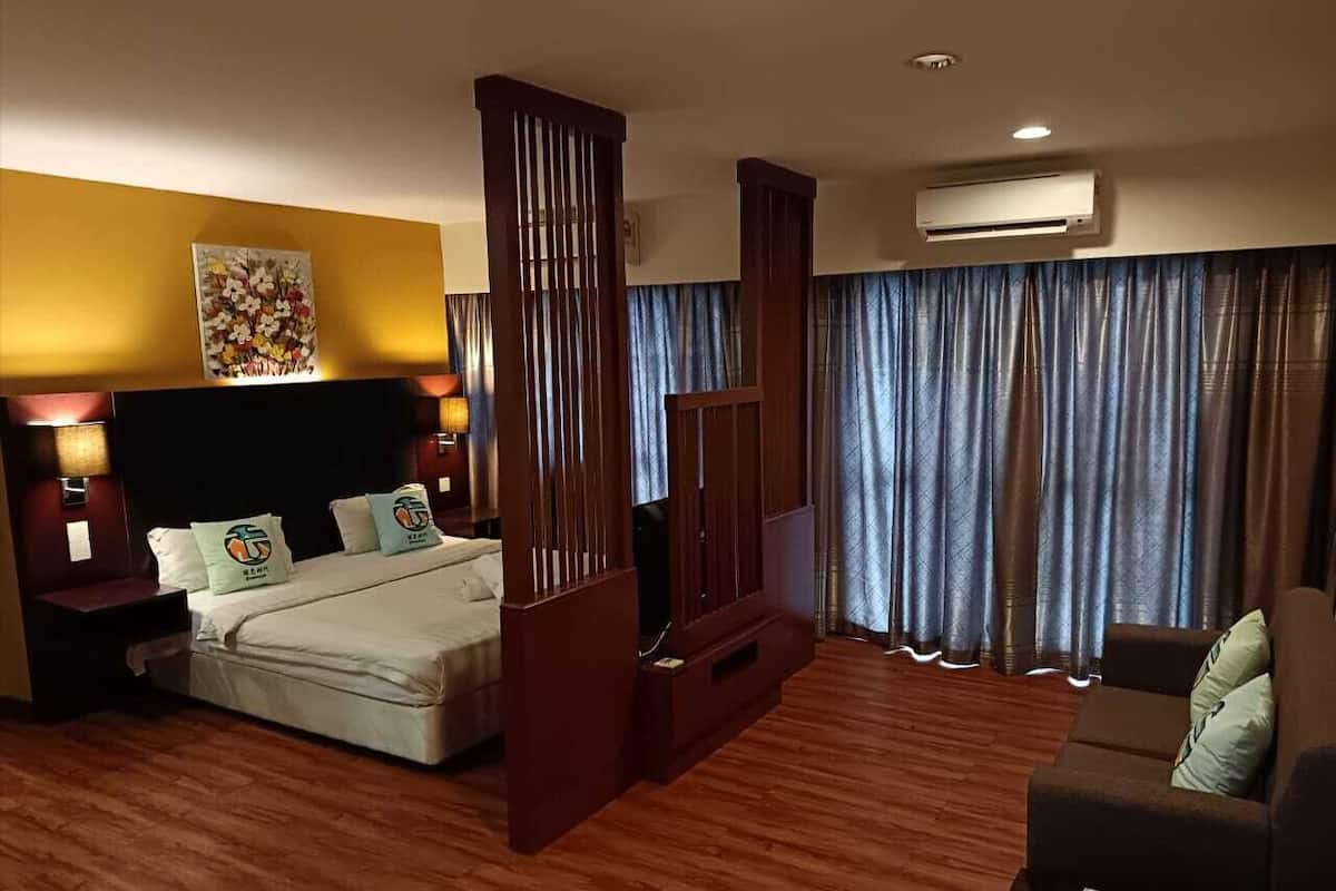 A hotel room with a bed, a TV, a sofa, a wooden partition, and a painting on the wall.