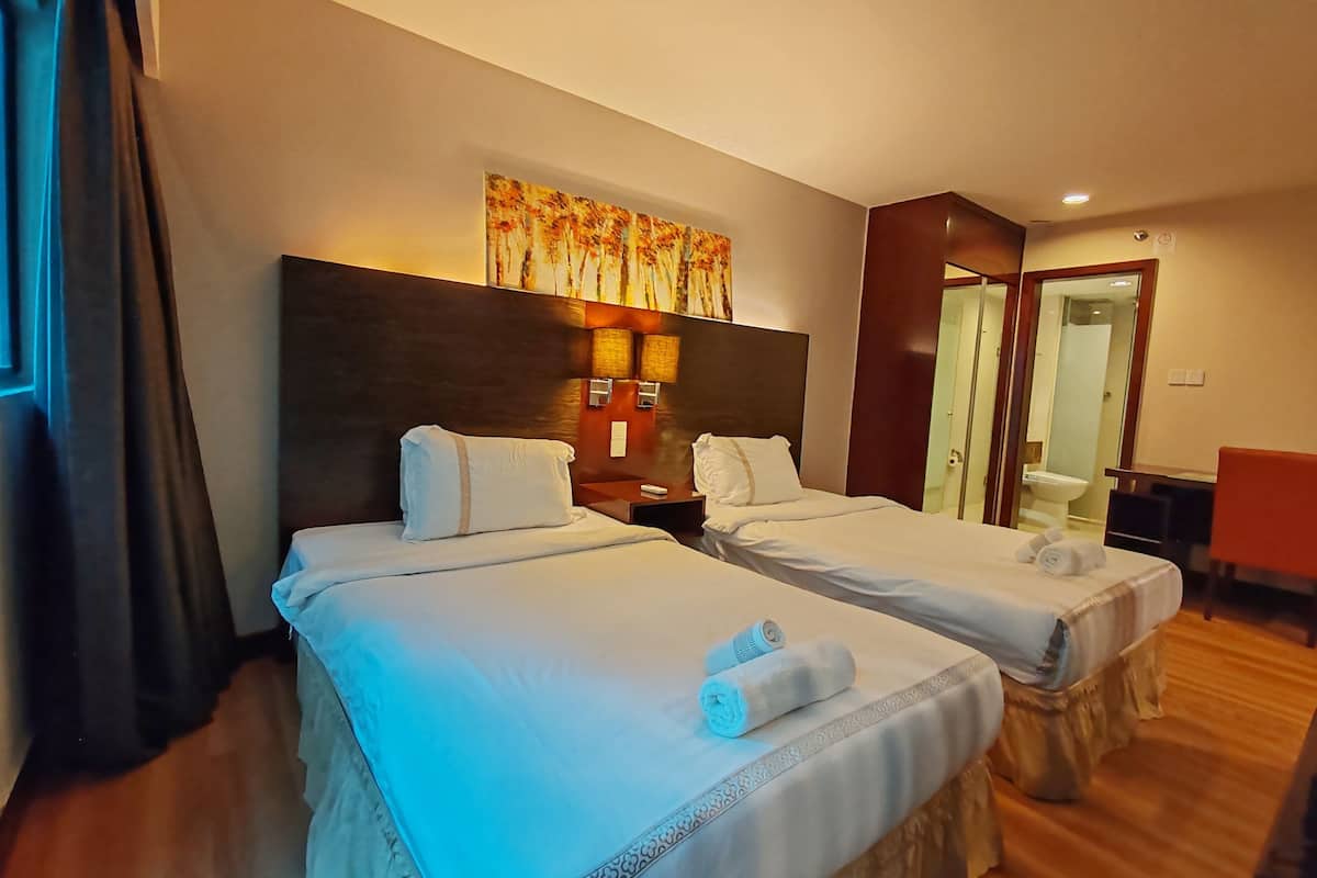 A hotel room with two beds, a painting above the headboard, a desk, and a bathroom visible through an open door.