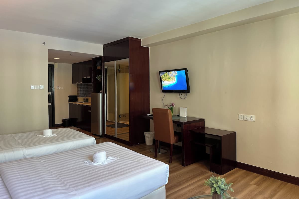 A hotel room with two beds, a desk, a television, and a small table with a plant.