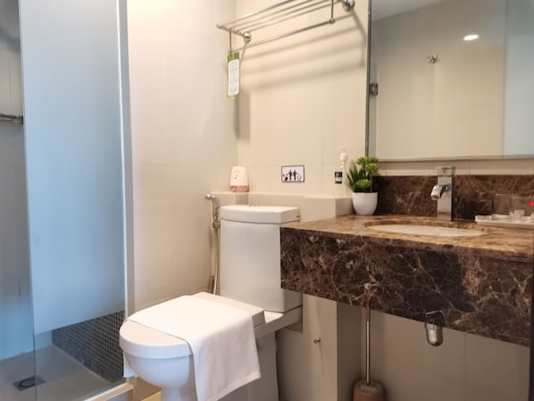Um banheiro moderno com bancada de mármore, vaso sanitário, chuveiro e pia.