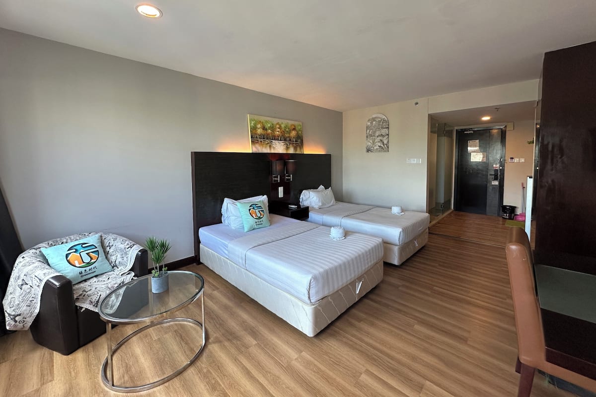 A hotel room with two beds, a glass table, a small seating area, and a wooden floor.