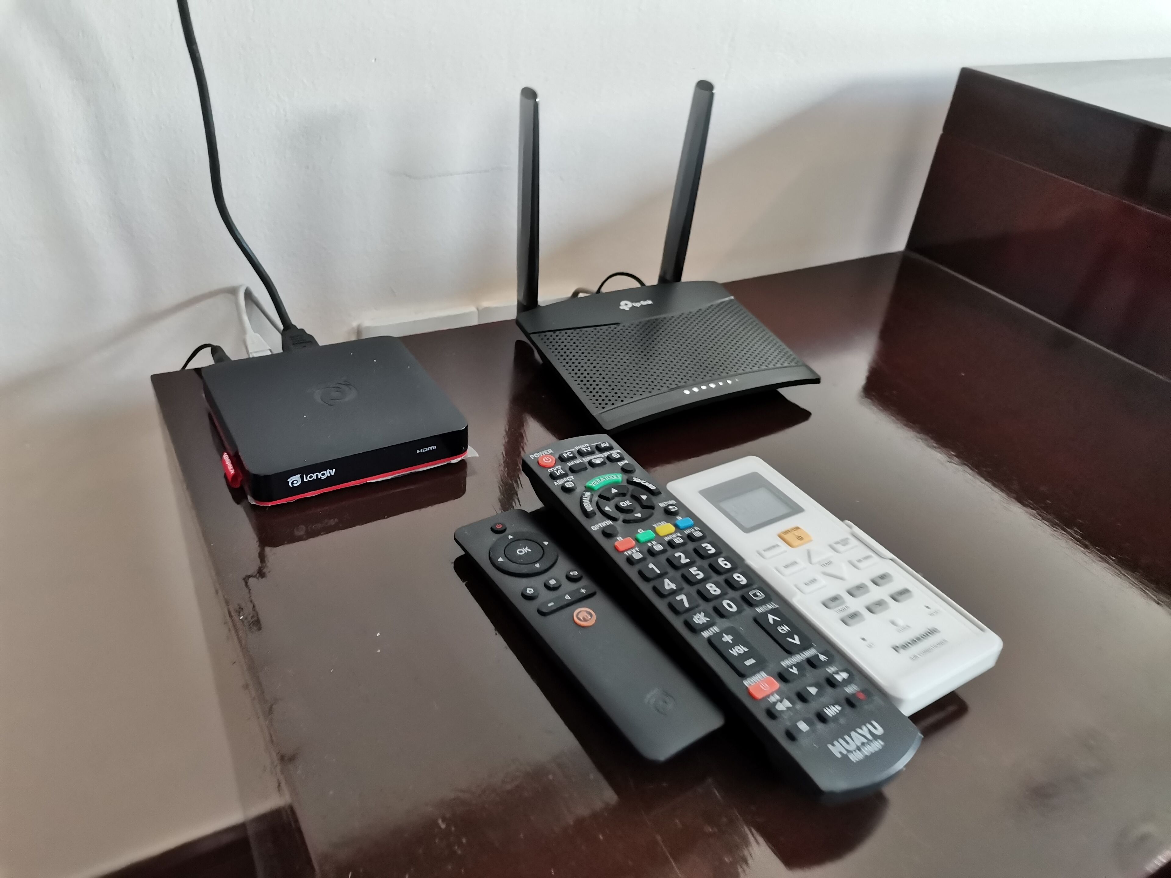 Et bord med en sort LongTV-boks, en sort router og to fjernbetjeninger.