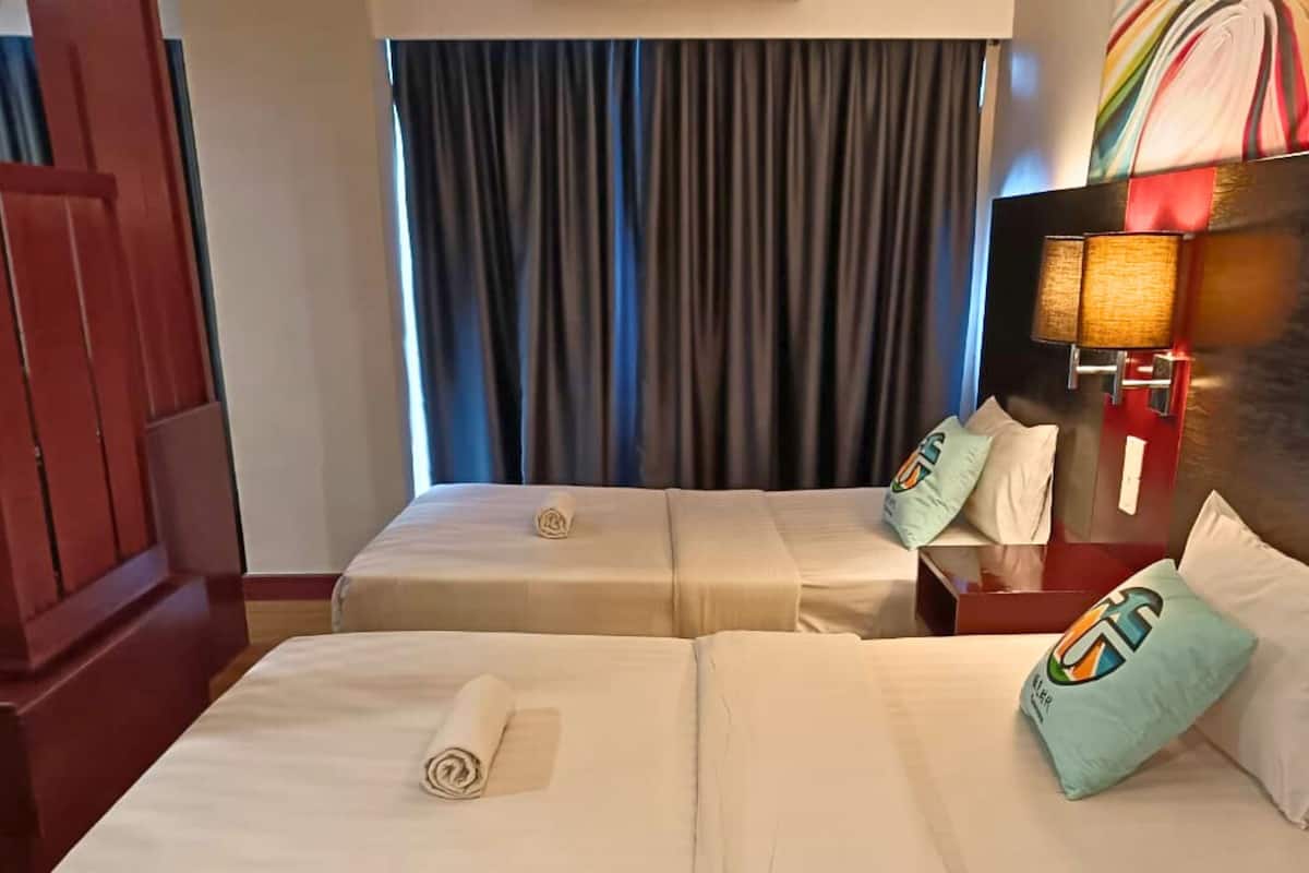 A hotel room with two beds, a wooden wardrobe, a lamp, and a painting on the wall.