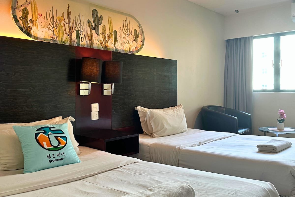 A hotel room with two beds, a large wall mural, a desk with a chair, and a window with curtains.