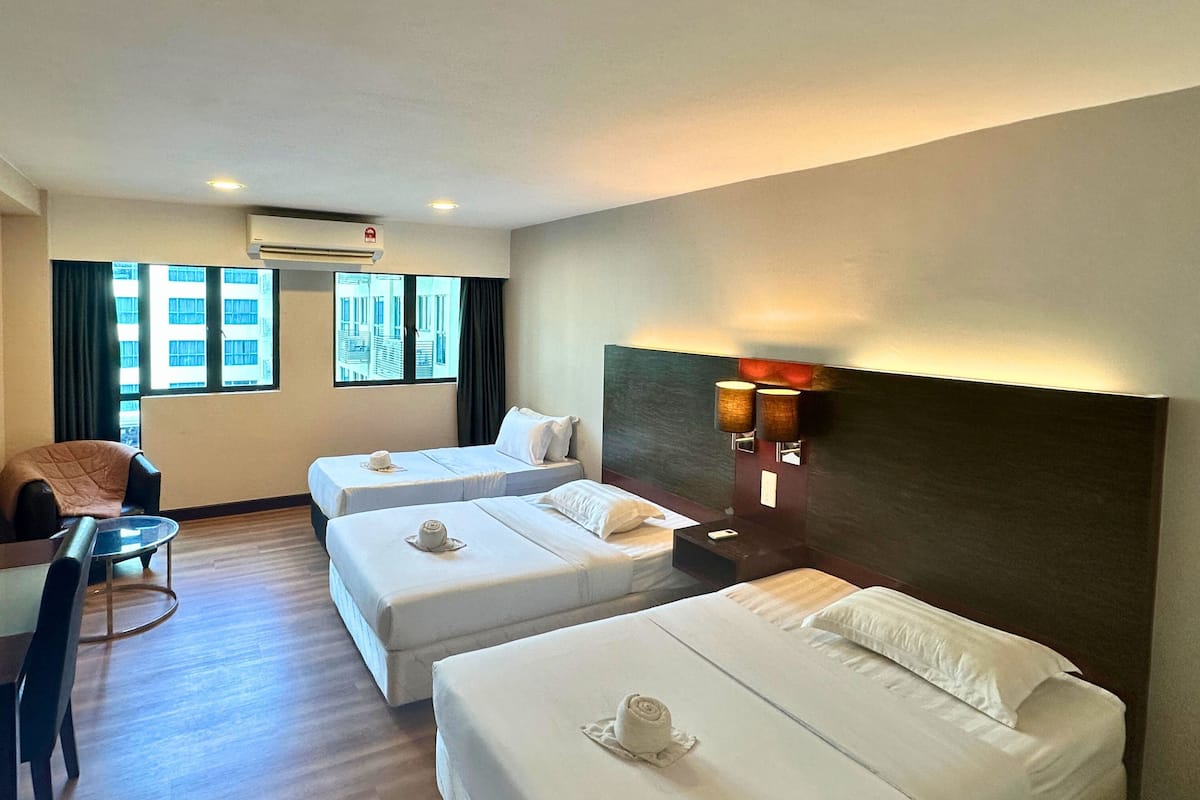 A hotel room with two single beds, a small table, a chair, and a view of the city through large windows.