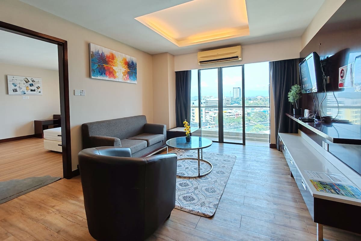 A modern living room with a sofa, armchair, coffee table, and a view of the city through large windows.