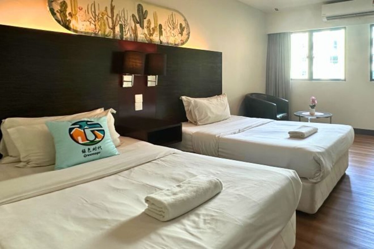 A hotel room with two beds, a headboard with a cactus mural, a small table with a vase, and a window with curtains.
