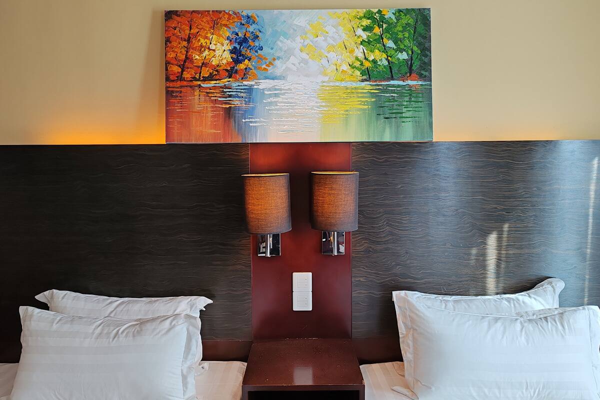 A hotel room with a large painting of a landscape above the bed, two bedside lamps, and a nightstand.