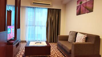 A hotel room with a sofa, a coffee table, a TV, and a large window with curtains.