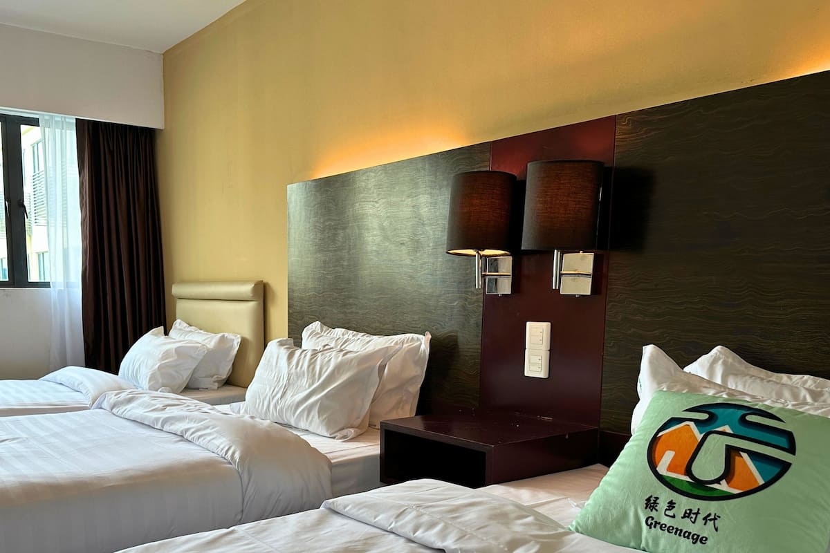 A hotel room with two beds, a nightstand, and a wall-mounted lamp.