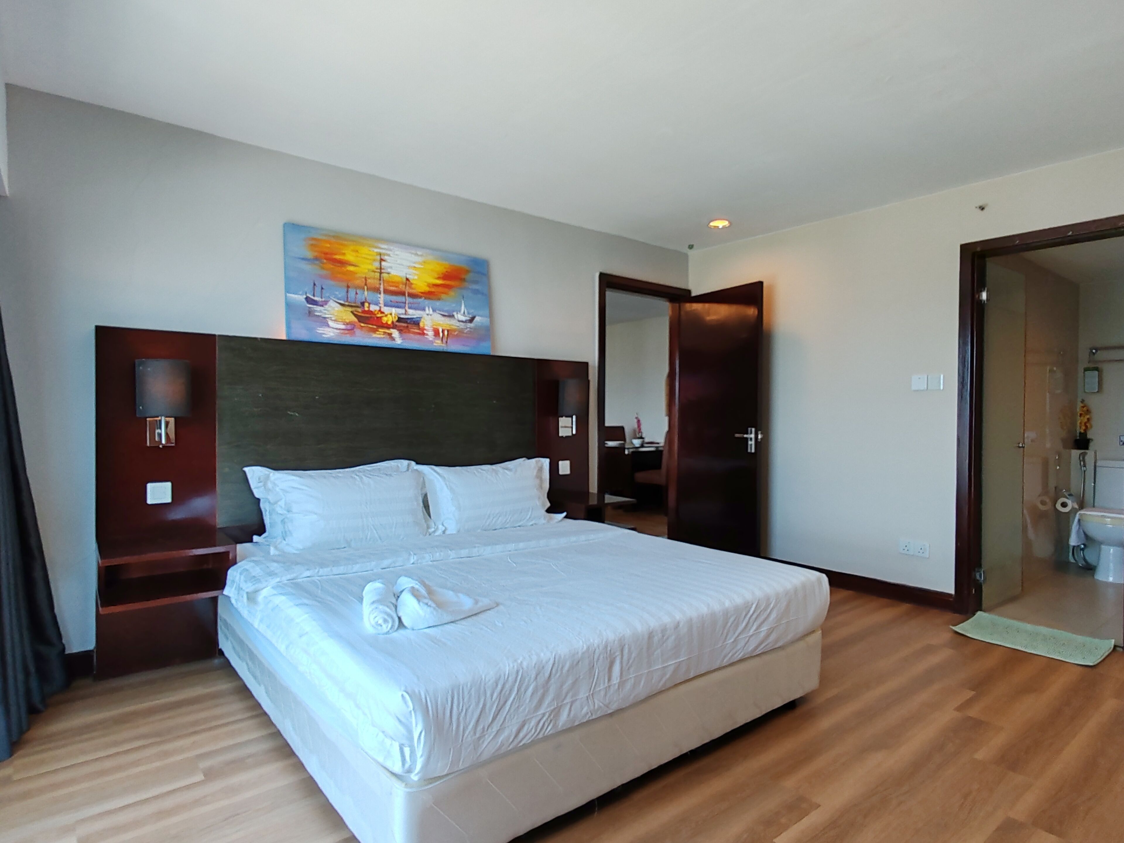A hotel room with a large bed, a headboard with artwork, a nightstand, and a bathroom visible through an open door.