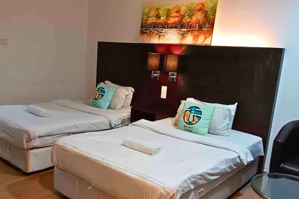 A hotel room with two beds, a small table, and a painting on the wall.