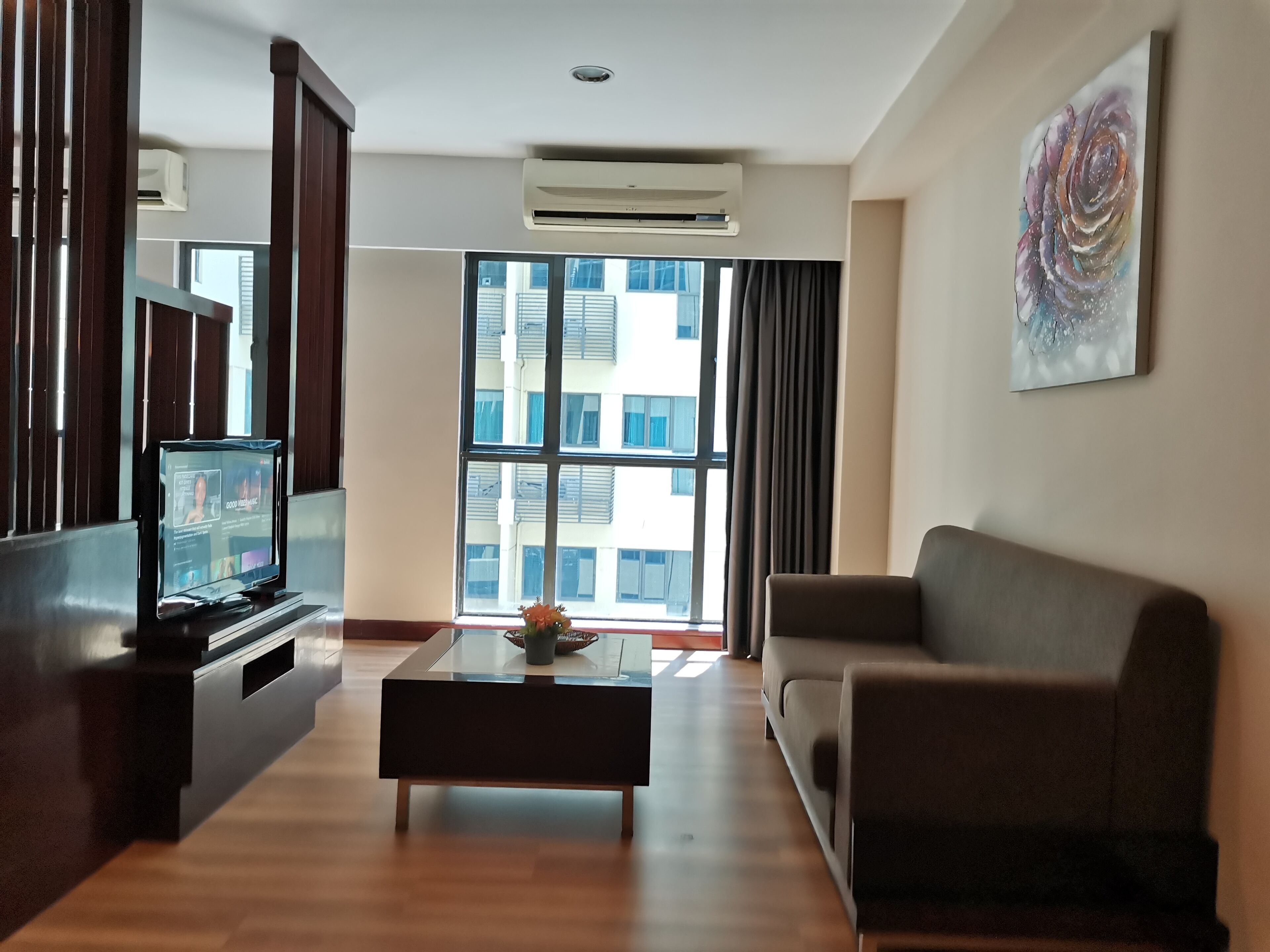 Una sala de estar moderna con un televisor de pantalla plana, una mesa de centro con un florero, un sofá y un ventanal con cortinas.
