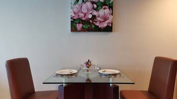 A dining table with two chairs, a glass top, and a floral painting above it.