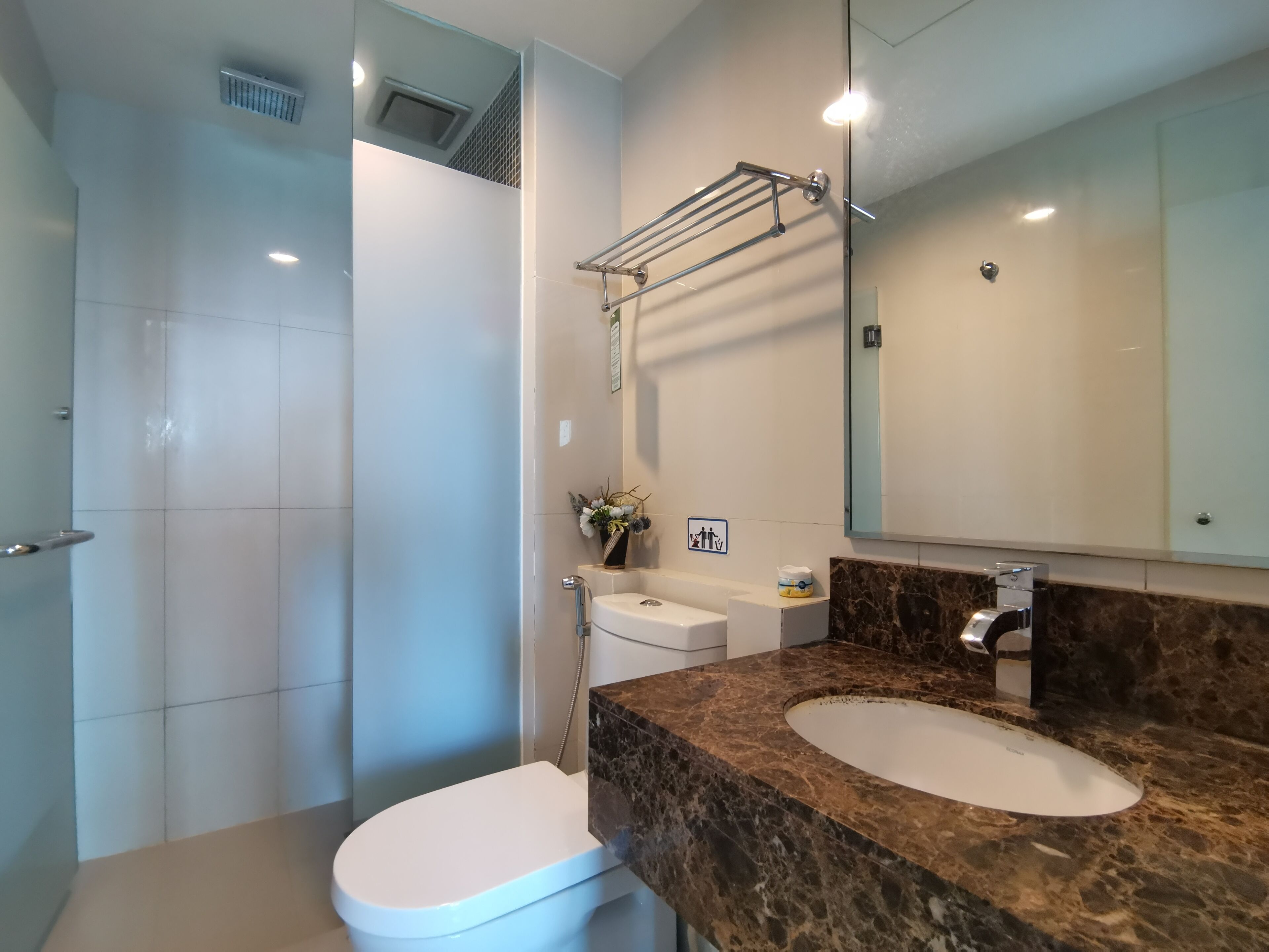 A modern bathroom with a white toilet, a shower, a marble sink, and a large mirror.