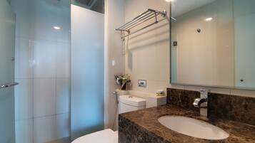 A modern bathroom with a white toilet, a shower, a marble sink, and a large mirror.