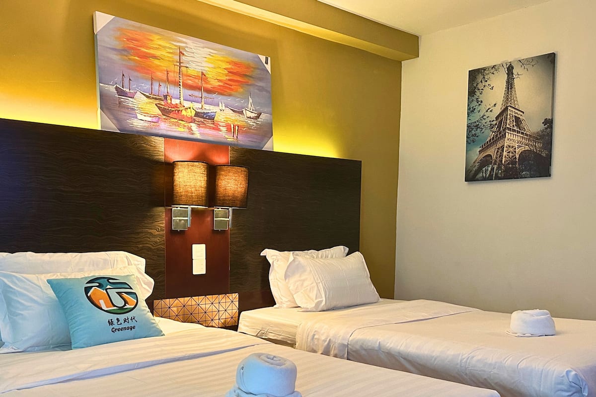 A hotel room with two beds, a headboard with wall-mounted lamps, a painting of a sunset, and a picture of the Eiffel Tower.