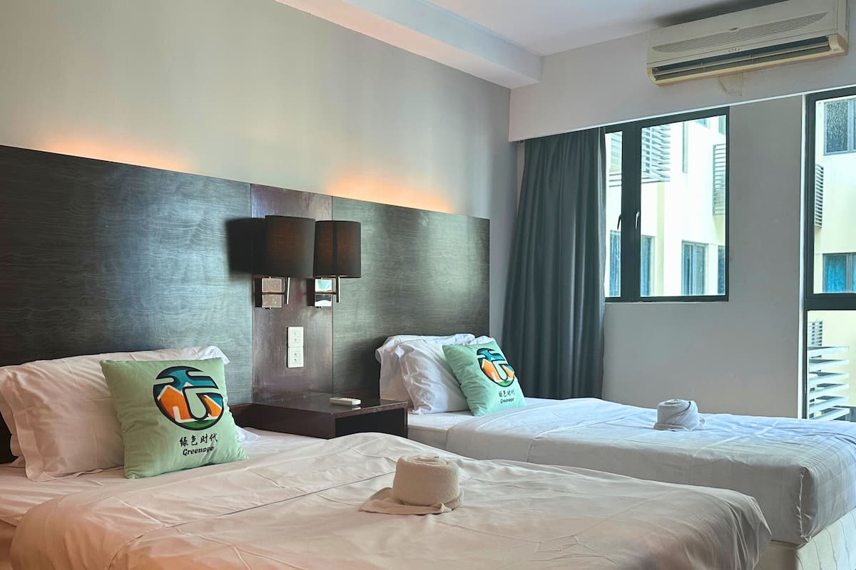 A hotel room with two beds, a nightstand, a wall-mounted lamp, and a window with curtains.