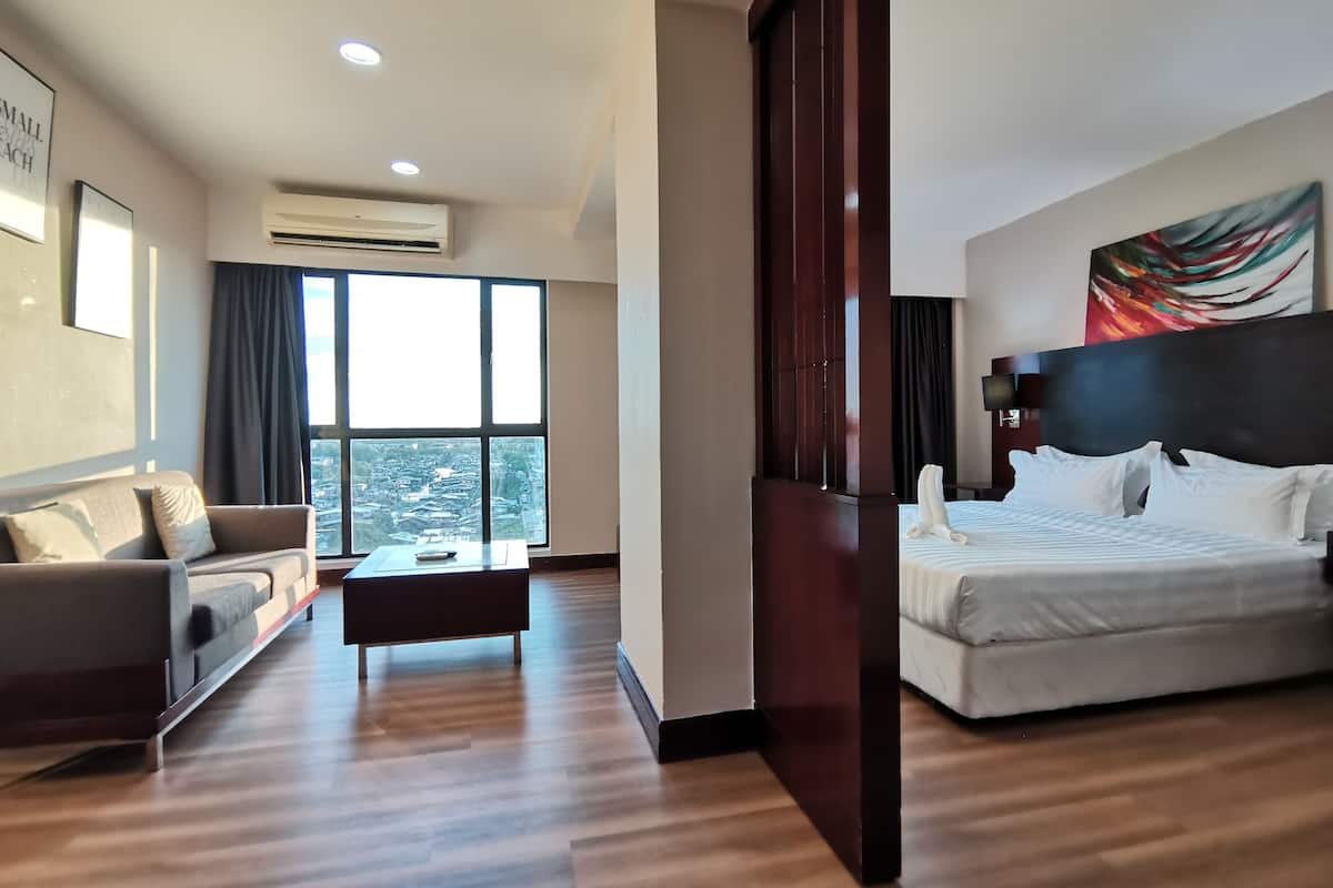 A hotel room with a bed, a sofa, a coffee table, and a large window offering a city view.