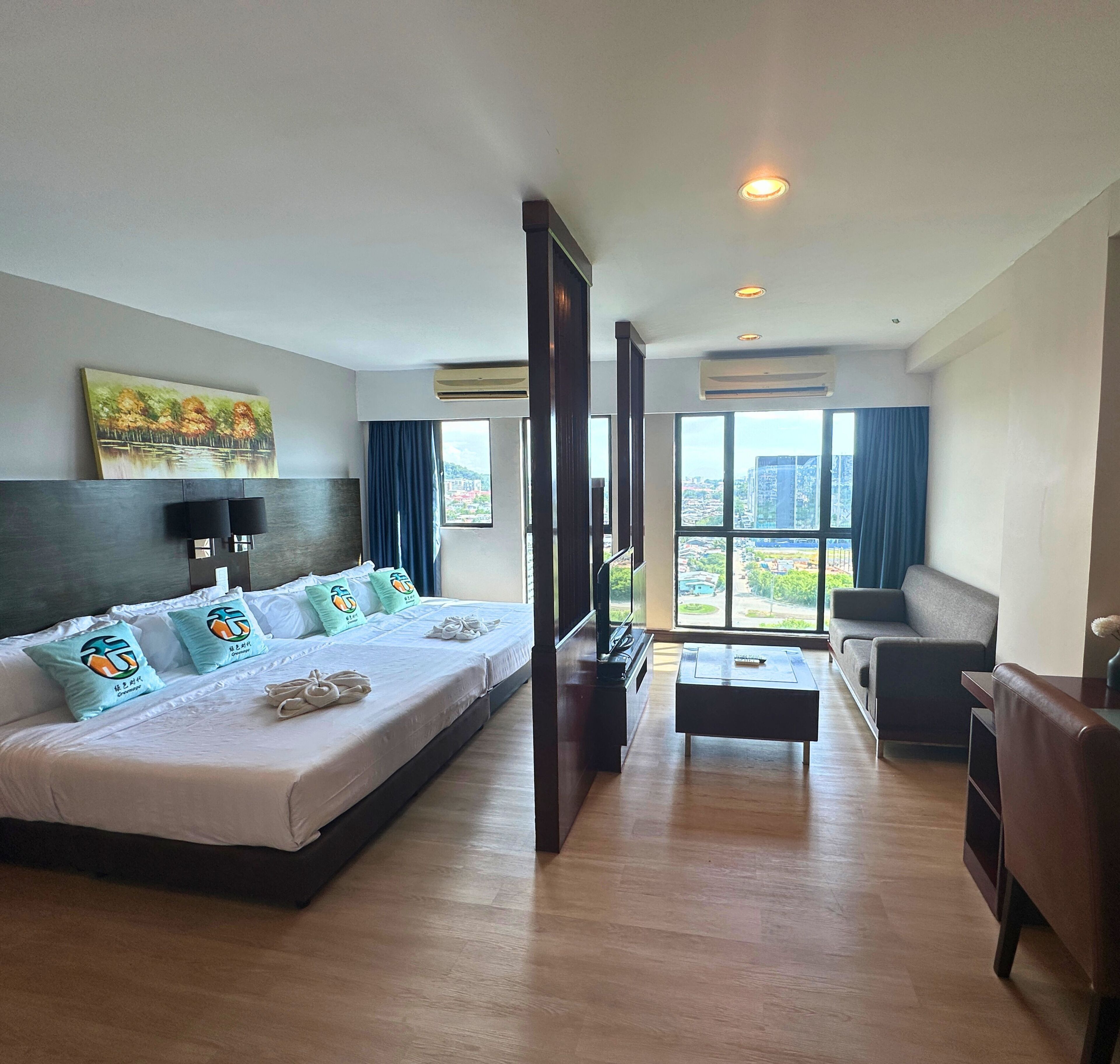 Habitación de hotel con una cama grande, televisión, sofá y balcón con vista a la ciudad.