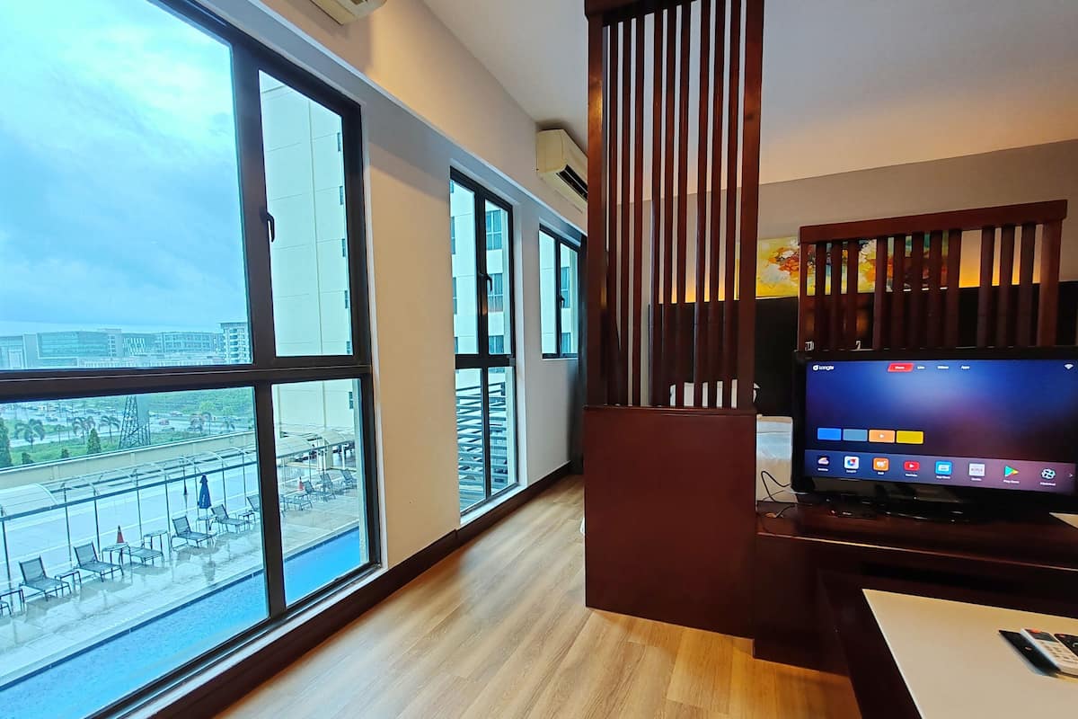 A modern hotel room with large windows, a wooden floor, a TV, and a desk.