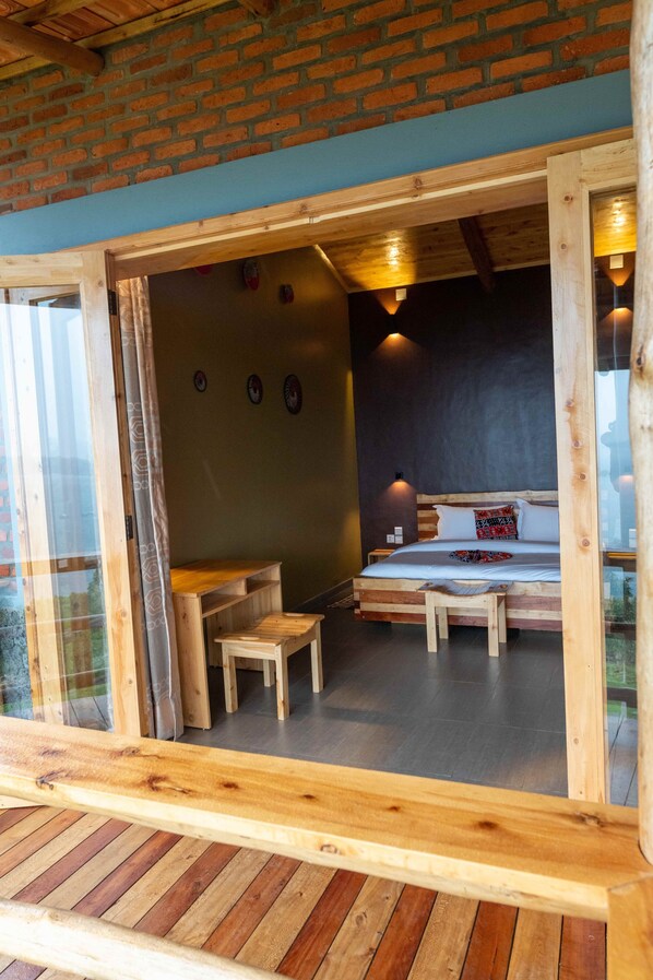 A wooden-framed room with a bed, a small table, and a bench. - Umutuzo Lodge Kivu Lake (Boneza)