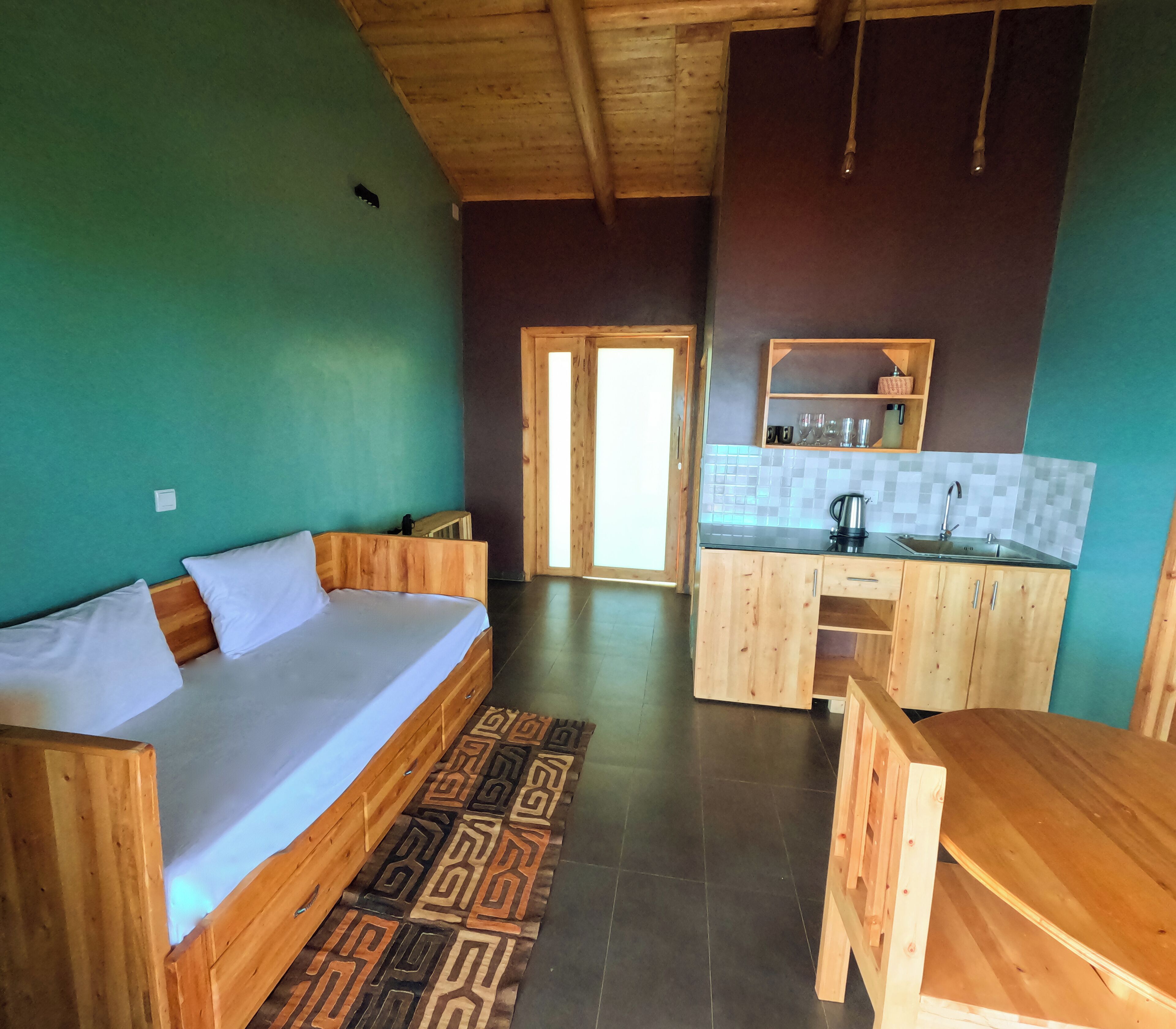 A wooden room with a bed, a small kitchen area, and a view of the outside.
