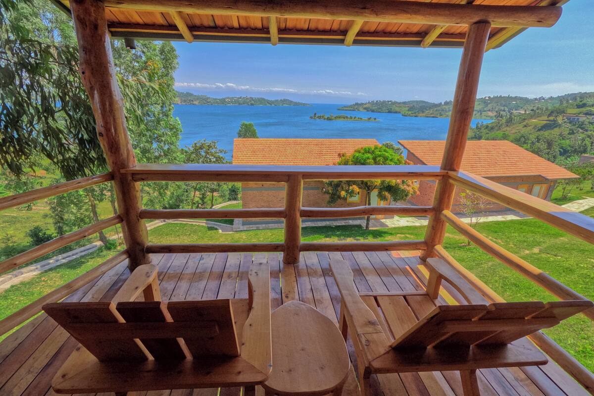 A wooden deck with two wooden tables and benches, overlooking a scenic view of a lake and surrounding greenery.