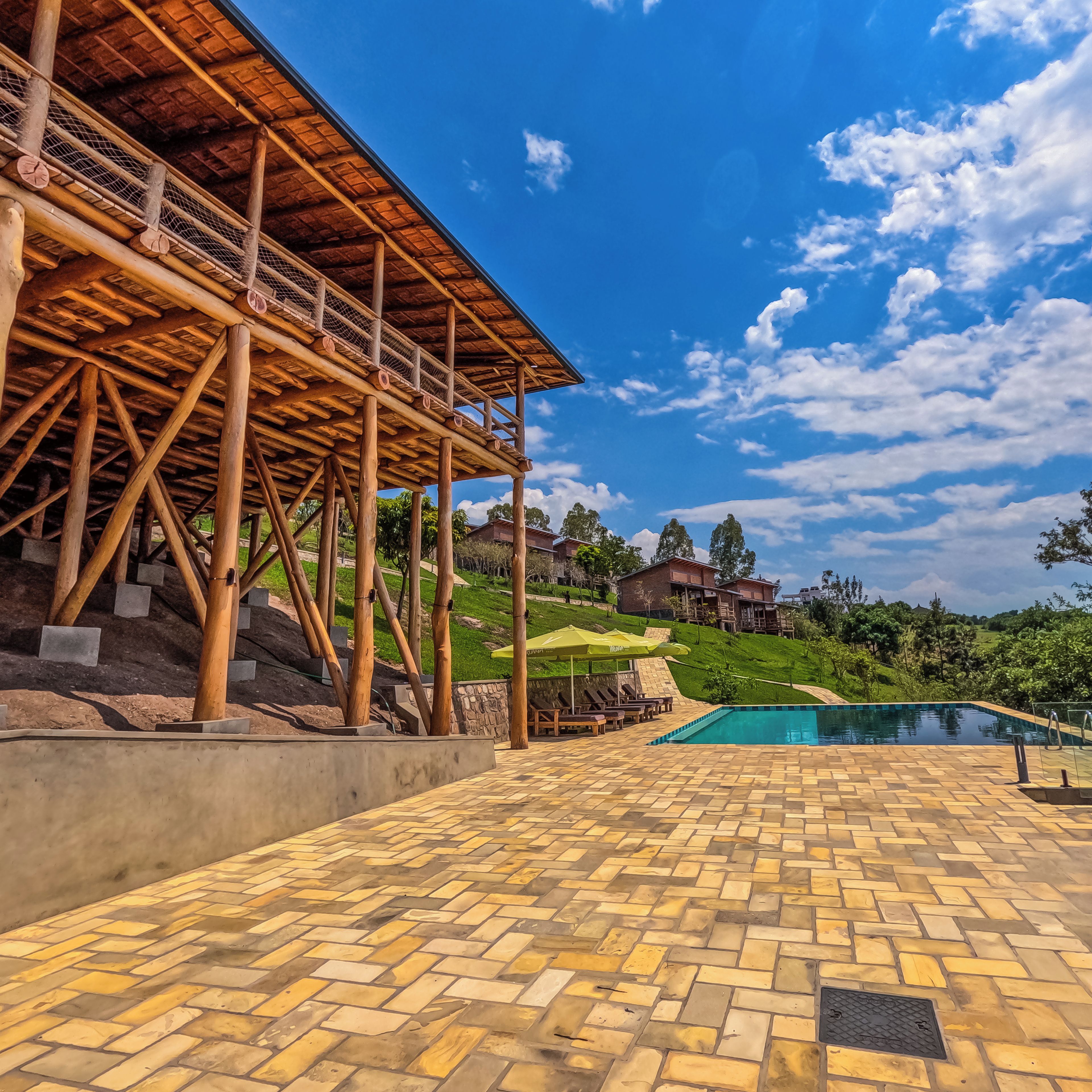 A pool area with a tiled floor, wooden deck, and a view of a hillside with houses.