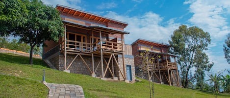 Un edificio de dos pisos con fachada de piedra y balcones de madera, rodeado de césped y árboles.